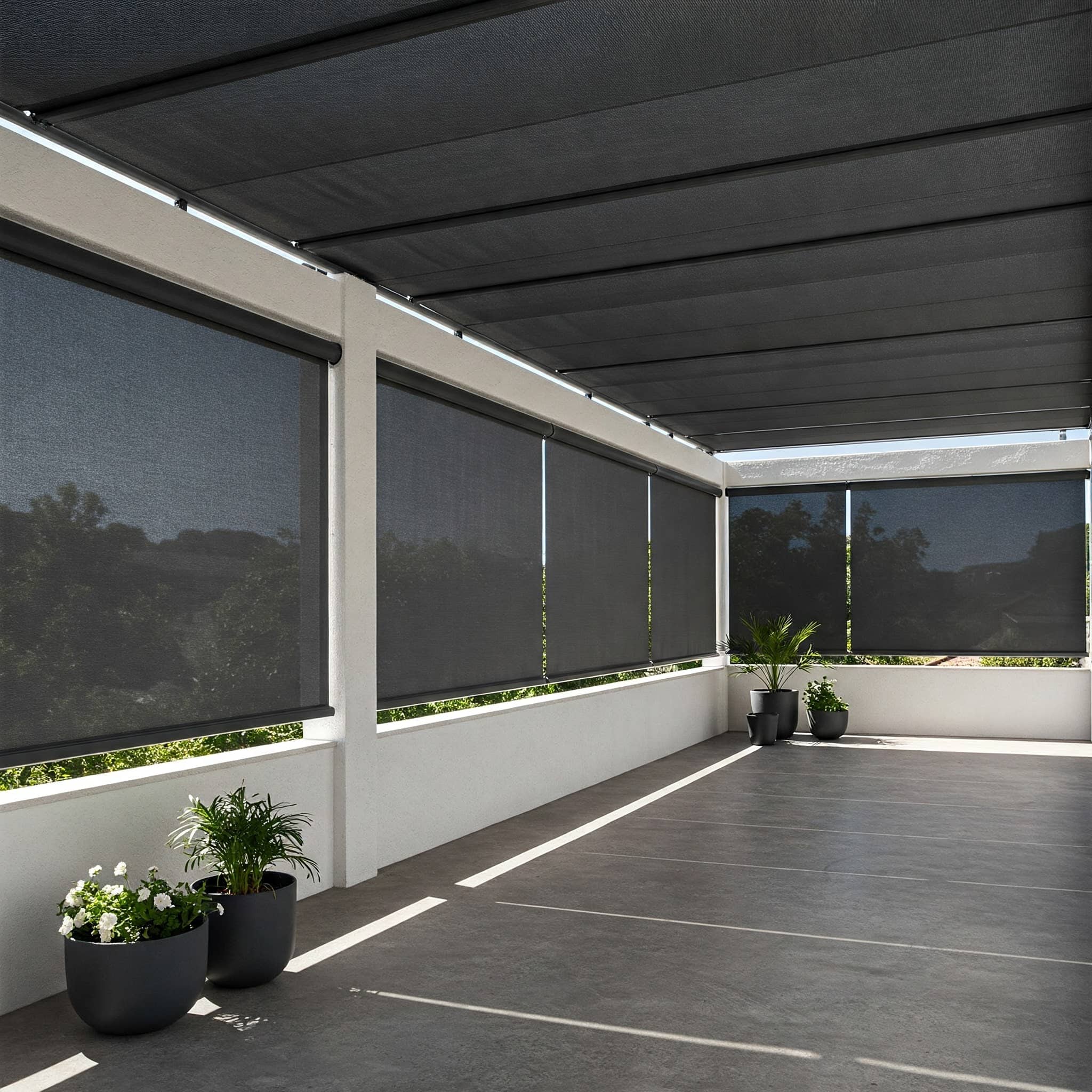 A spacious patio with a concrete floor, partially enclosed by white columns and covered by dark exterior window shades. Several potted green plants are arranged along the edges, and trees are visible outside.