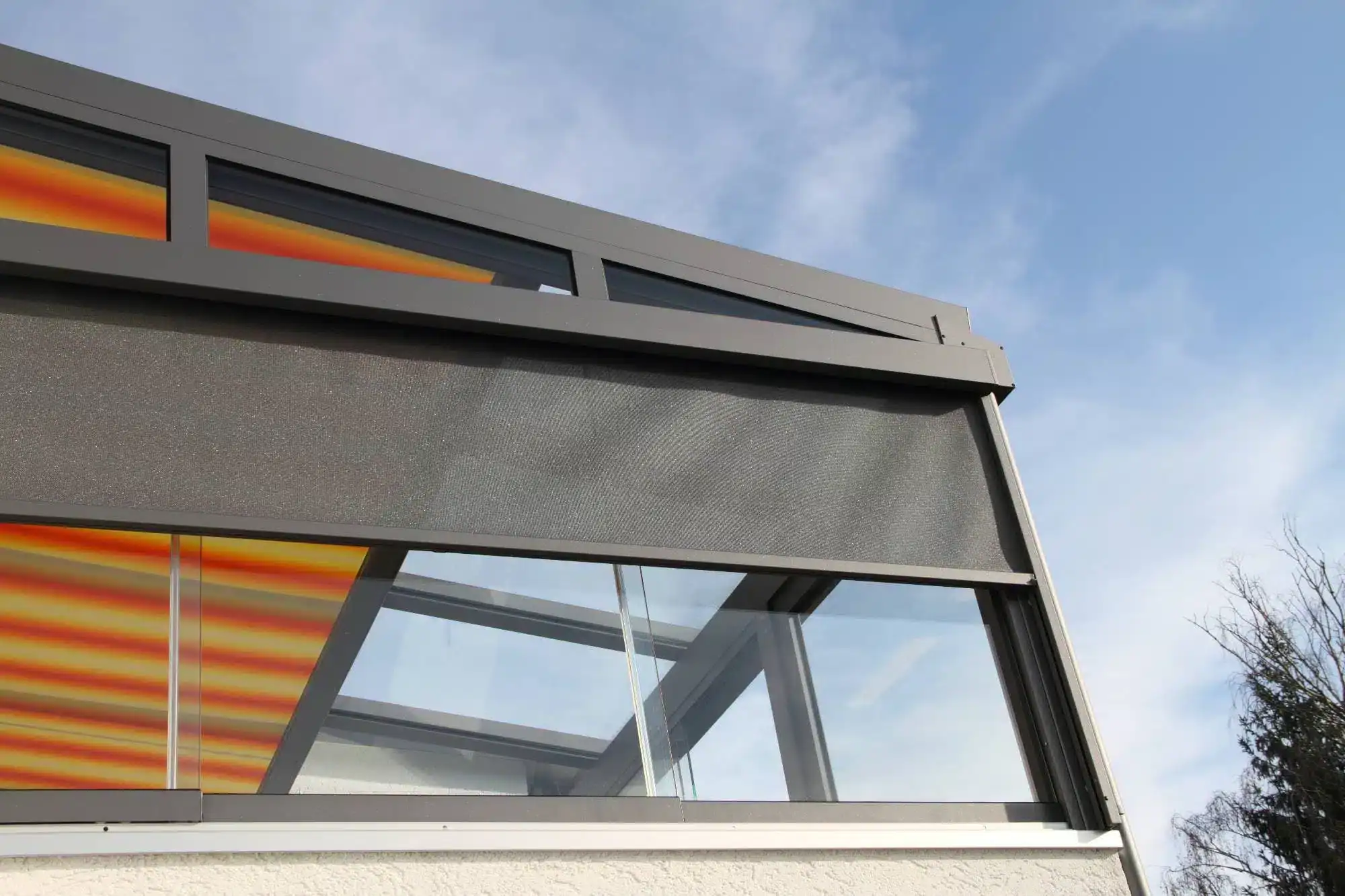 Close-up view of a modern glass building facade with horizontal window shades, featuring innovative windows treatments Miami-Dade County, FL, including a partially lowered mesh screen and striped yellow-red awnings set against a blue sky.