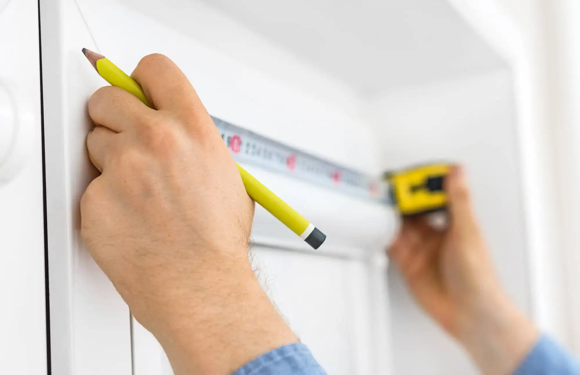 A person measures a window frame with a measuring tape and marks the measurement on the white wall, preparing for windows treatments in Miami-Dade County, FL.