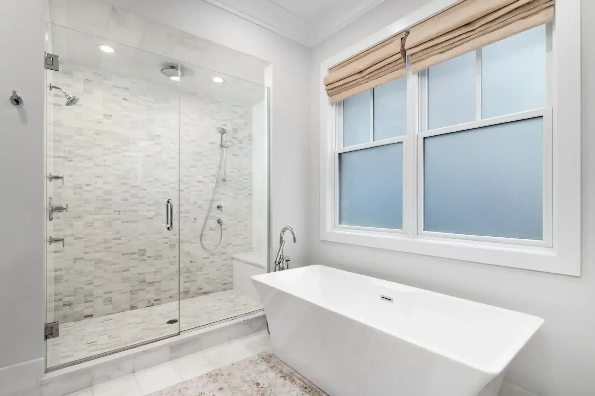 Modern bathroom with a glass-enclosed shower featuring tiled walls and a handheld showerhead, a white rectangular soaking tub, frosted double windows with beige blinds—perfect for those seeking stylish window treatments in Miami-Dade County, FL.
