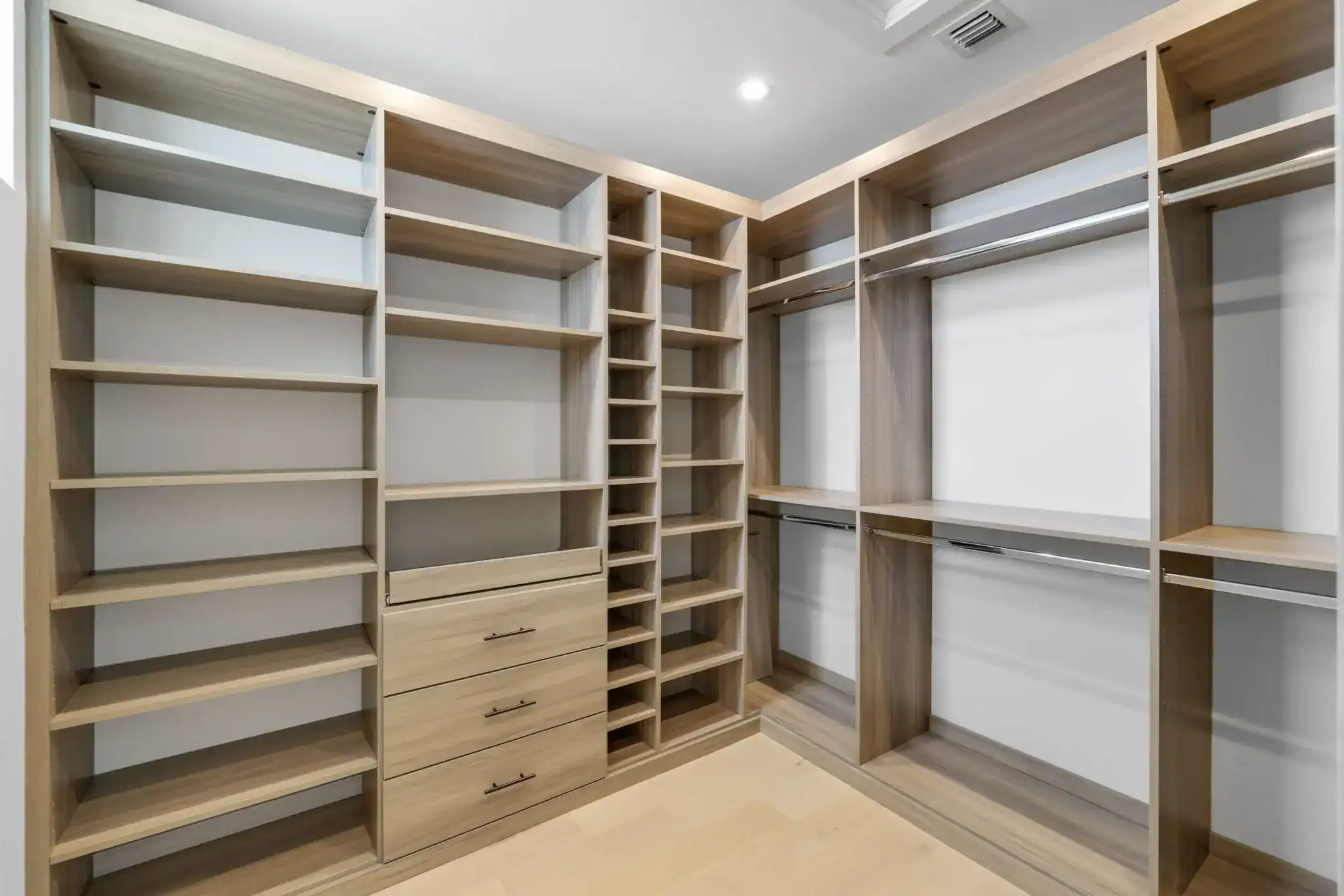 Spacious walk-in closet with light wood shelving, drawers, and hanging rods, designed for organized storage. The open shelves and ample space create a modern, clean look under bright ceiling lighting—perfect for any FL home.