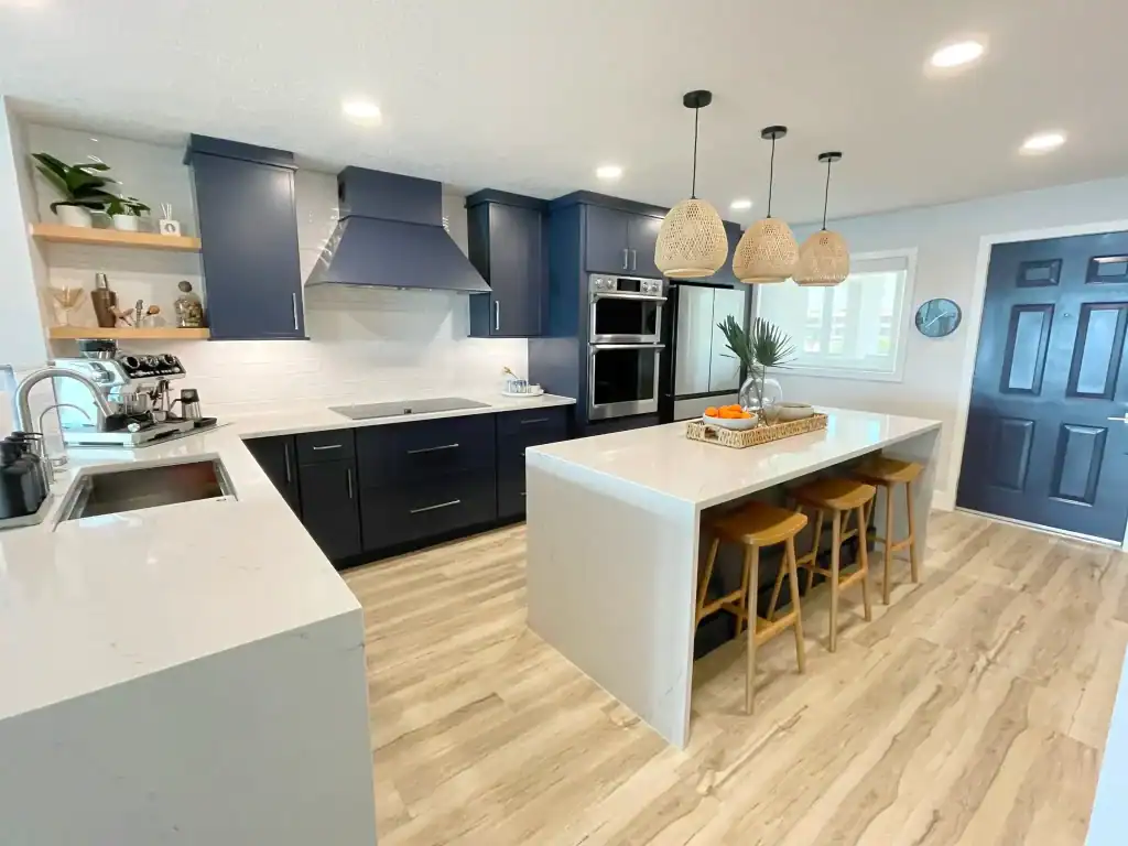 Modern kitchen with navy blue cabinets, white marble countertops, stainless steel appliances, and a spacious island—perfect inspiration for kitchen remodeling in Miami-Dade County, FL. Elegant pendant lights and wood flooring add warmth and style.