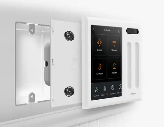 A smart home control panel is mounted on a wall with its front cover open, revealing screws inside. The screen displays options for controlling lights, shades, climate, and access.