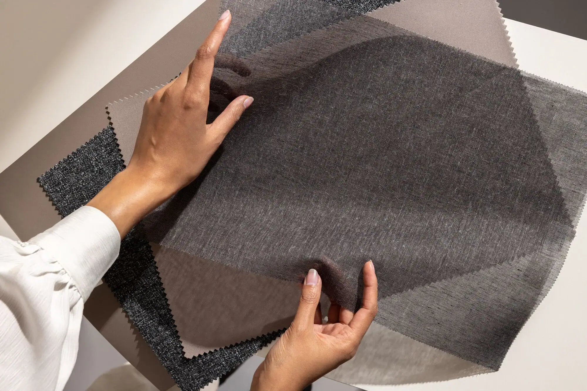 Person handling translucent fabric samples on a table.
