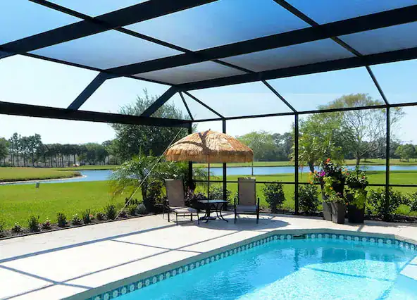 Backyard pool enclosure with two chairs, table, and lake view.