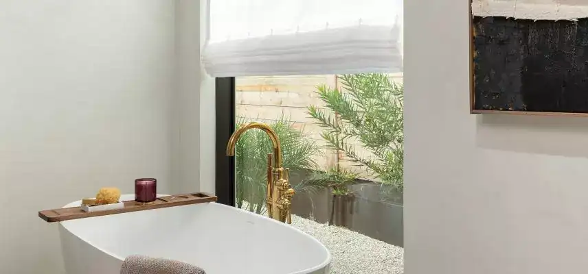 Luxurious white bathtub with gold faucet and natural light.