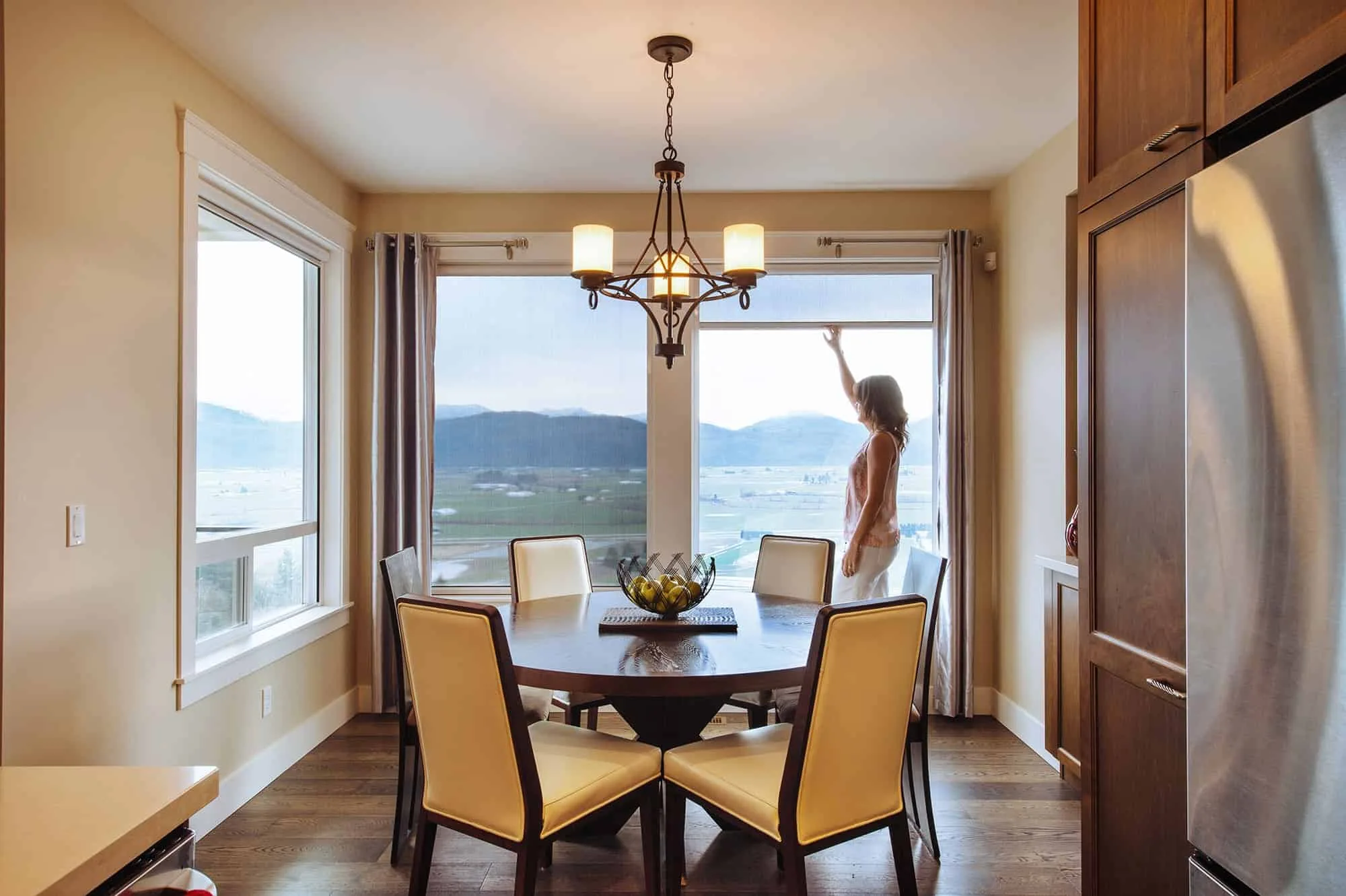 Woman adjusting blinds in a dining room with a panoramic window view.