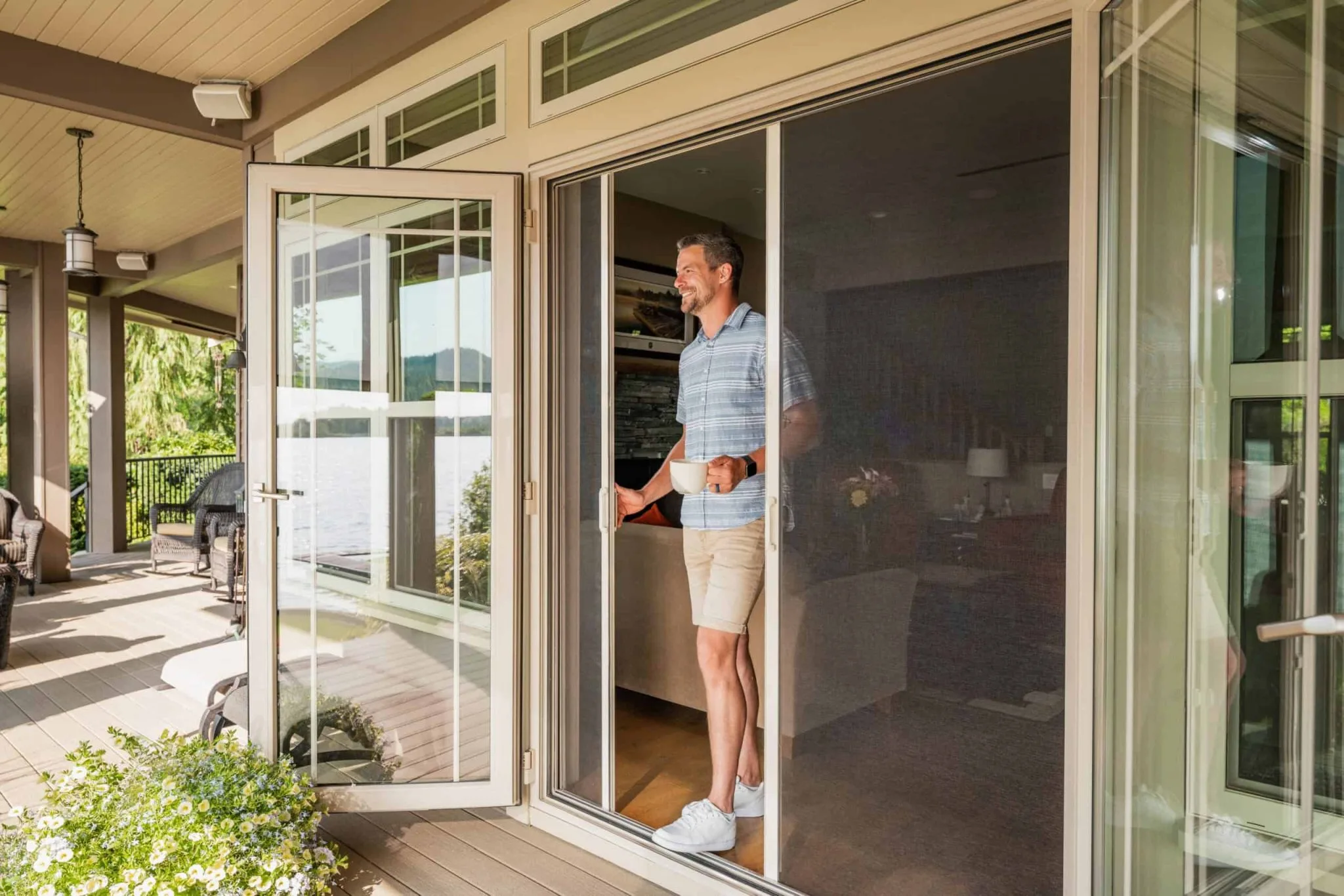 Man holding coffee cup standing by open patio screen door