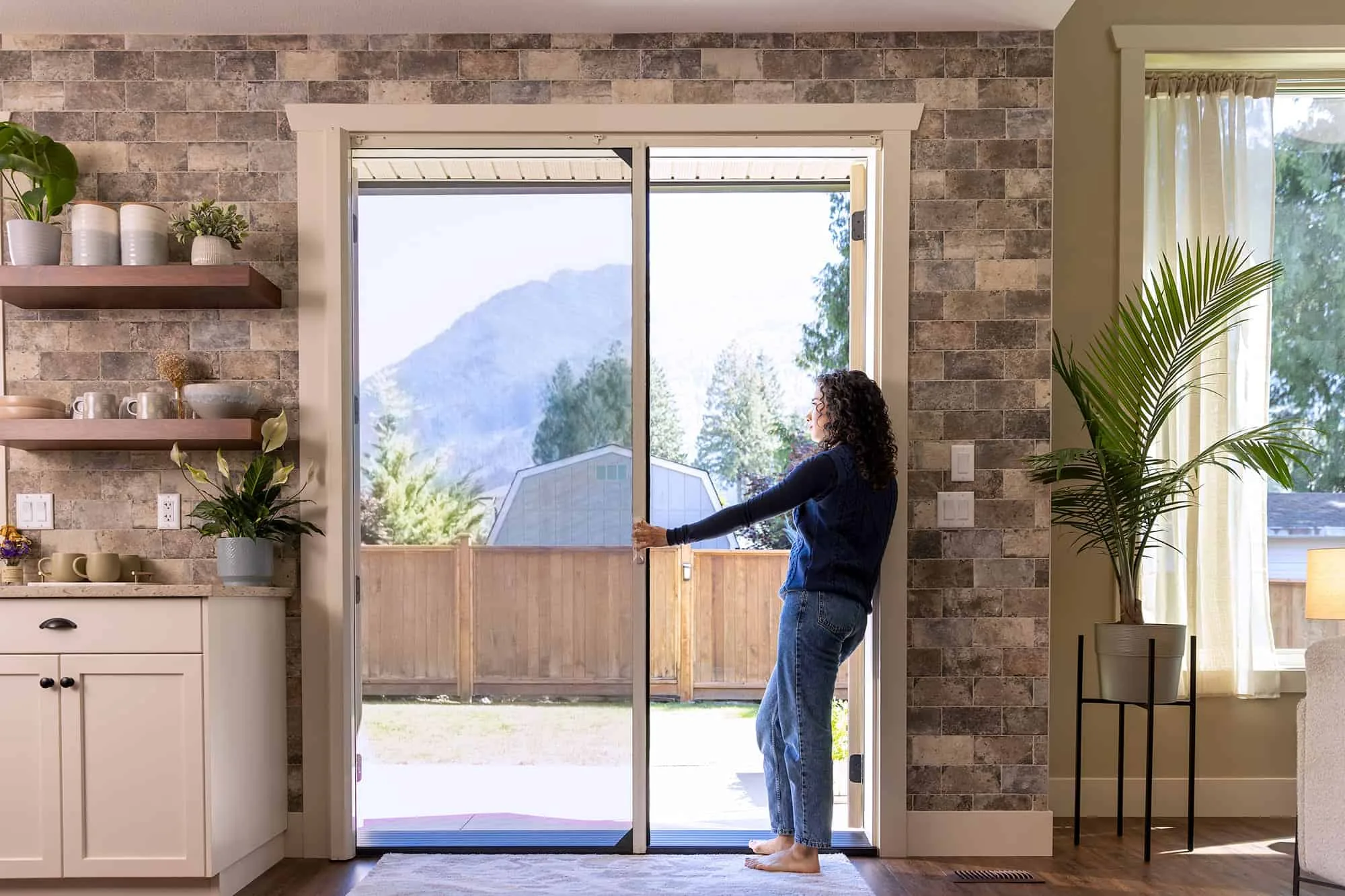 Woman in blue sweater opening a sliding glass door revealing mountain scenery.