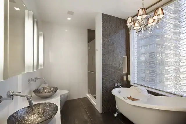Modern bathroom featuring a freestanding bathtub, two vessel sinks with textured basins, a glass-enclosed shower, and a chandelier. This stylish Broward County space highlights neutral tones and elegant finishes&mdash;an Interior Exterior Custom Design masterpiece.