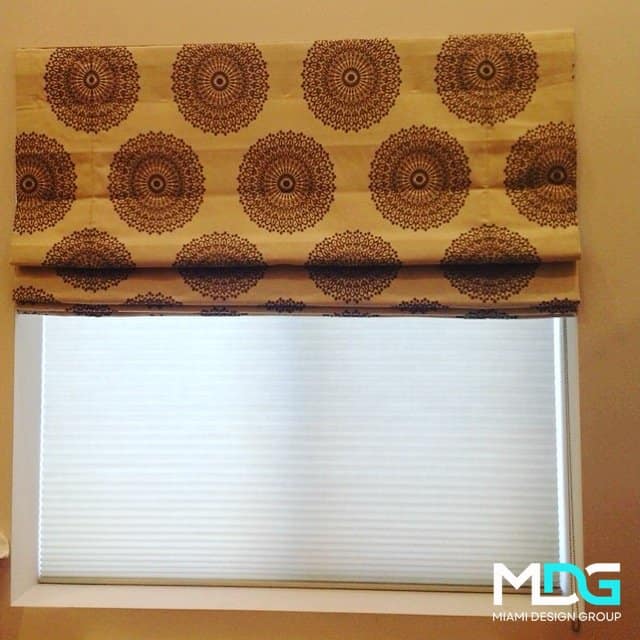Roman shade with brown circular patterns tops white blinds, showcasing elegant window treatments in Miami.
