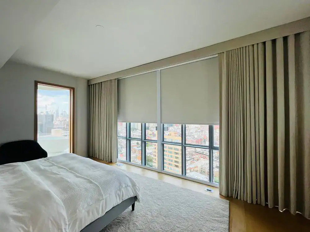Bedroom with full-length curtains framing two pale roller shades