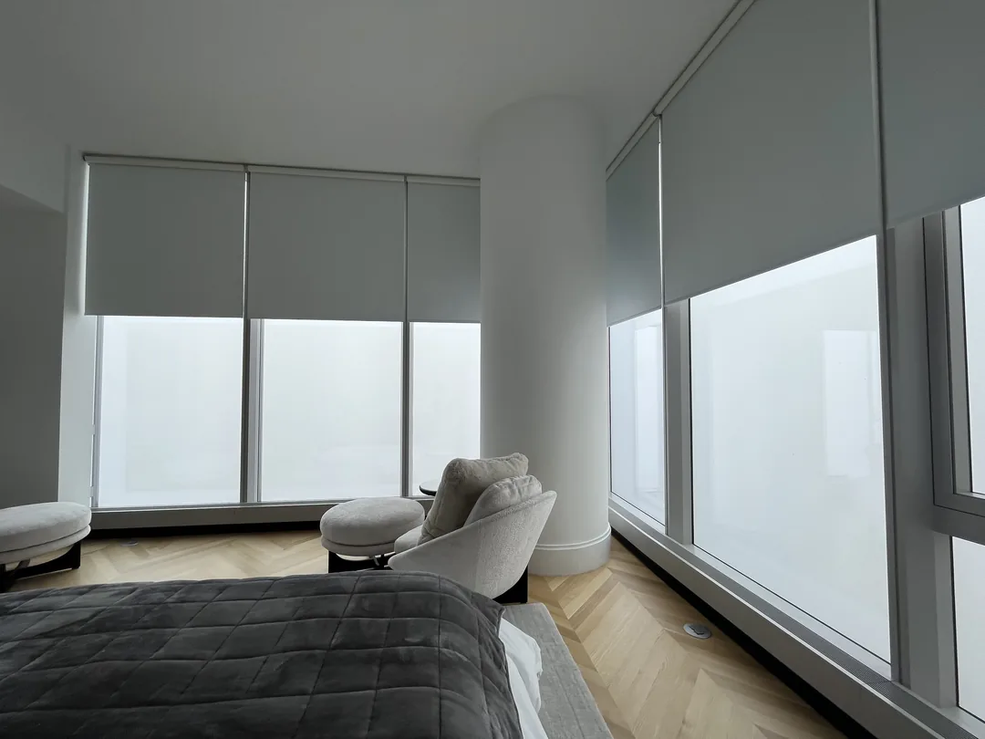 View across a bed toward two walls of roller shades