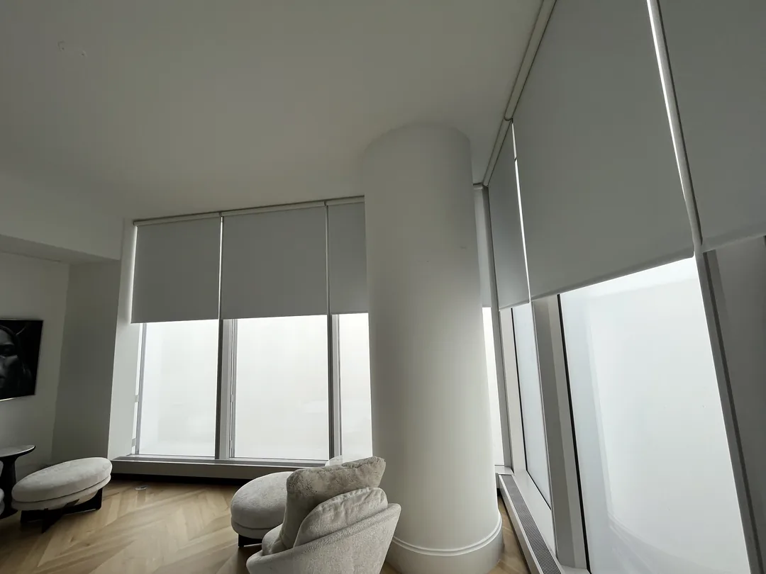 Corner windows with pale roller shades above an upholstered seating area