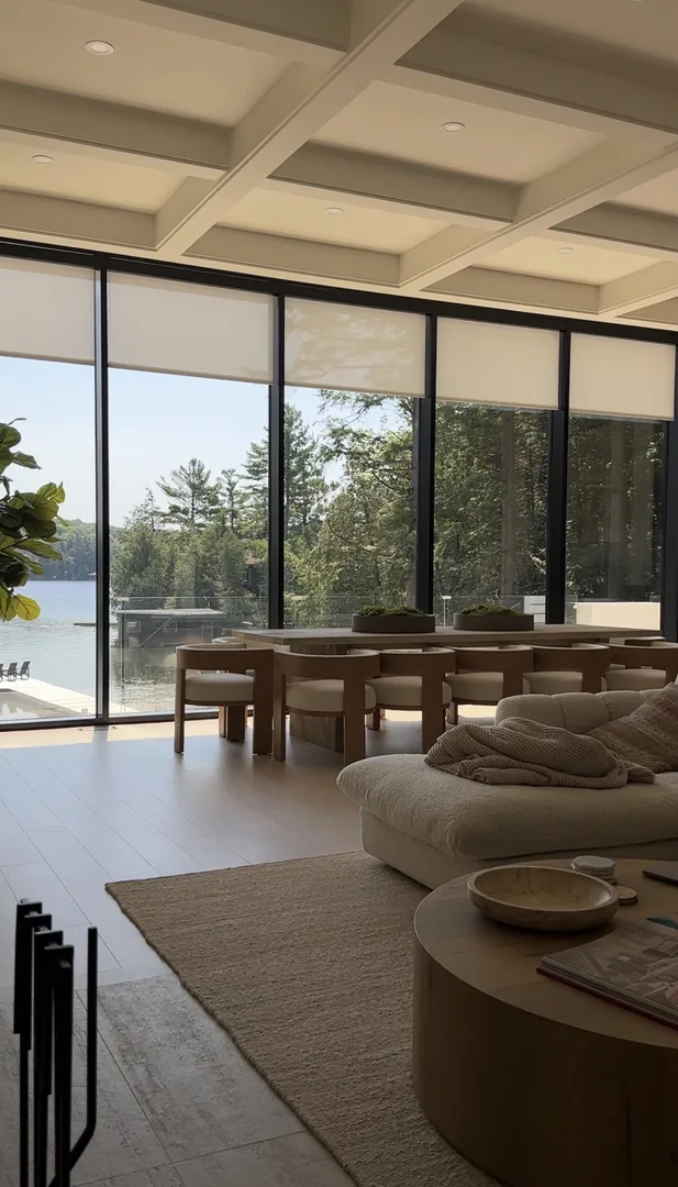 Living and dining area with tall black-framed windows and pale roller shades